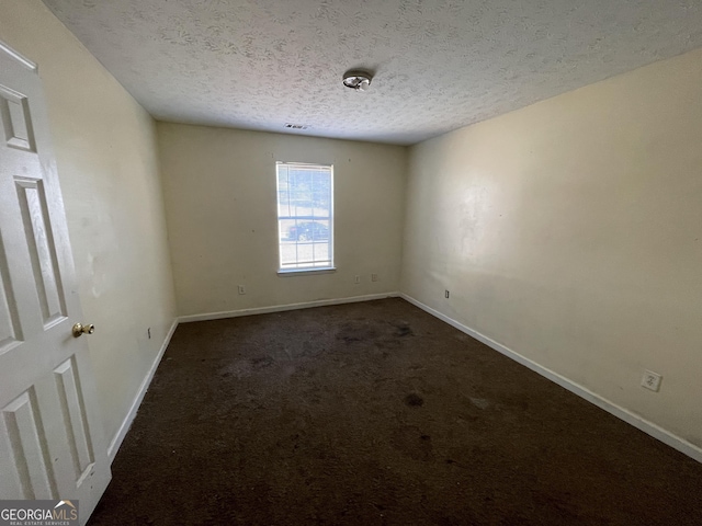 empty room featuring dark carpet and a textured ceiling