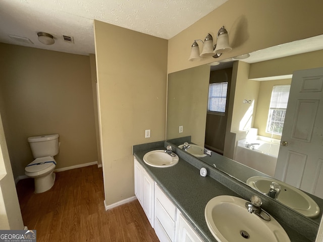 bathroom with hardwood / wood-style floors, a tub, vanity, toilet, and a textured ceiling