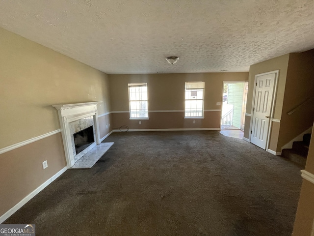 unfurnished living room featuring dark colored carpet, a textured ceiling, and a high end fireplace