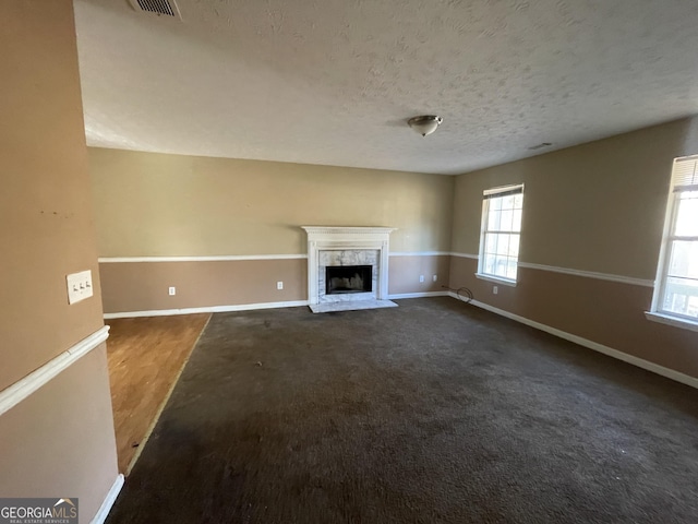 unfurnished living room featuring a premium fireplace, a textured ceiling, and dark colored carpet