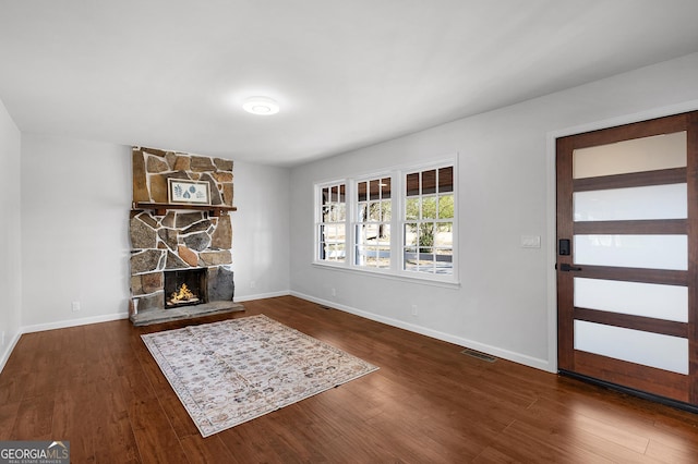 foyer entrance featuring dark wood-type flooring and a stone fireplace