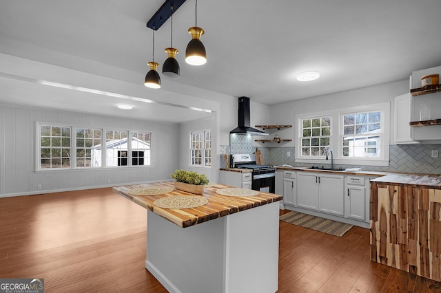 kitchen with wall chimney exhaust hood, sink, stainless steel gas stove, pendant lighting, and white cabinets