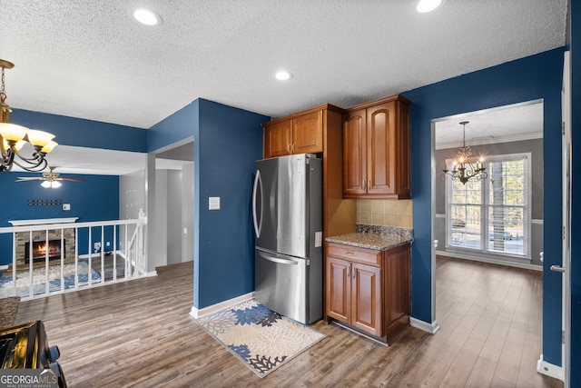 kitchen featuring pendant lighting, stainless steel fridge, light stone countertops, and dark wood-type flooring