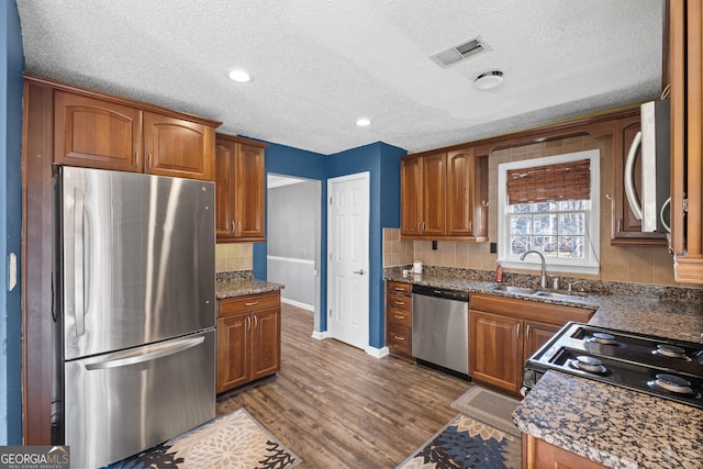 kitchen featuring appliances with stainless steel finishes, sink, dark stone counters, decorative backsplash, and dark wood-type flooring