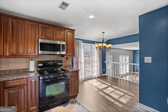 kitchen with black gas range, an inviting chandelier, tasteful backsplash, light hardwood / wood-style floors, and dark stone counters