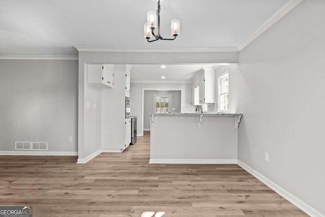 kitchen with white cabinetry, an inviting chandelier, light stone counters, light hardwood / wood-style floors, and kitchen peninsula