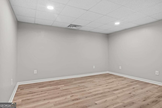 spare room featuring a drop ceiling and light hardwood / wood-style flooring