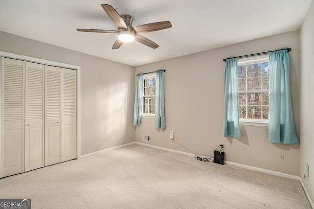 unfurnished bedroom with multiple windows, carpet flooring, ceiling fan, and a closet