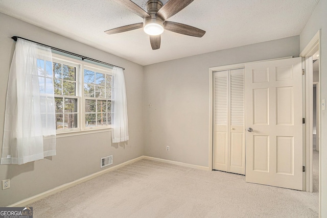 unfurnished bedroom featuring ceiling fan, light colored carpet, a closet, and a textured ceiling