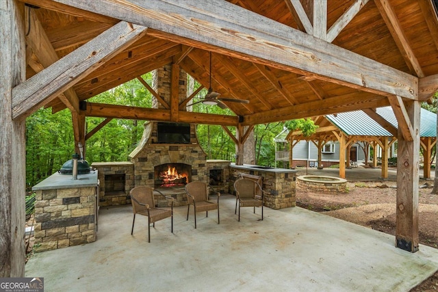 view of patio / terrace with ceiling fan, a gazebo, an outdoor stone fireplace, and an outdoor kitchen