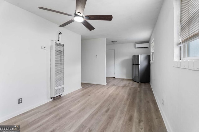 unfurnished living room with a wall mounted air conditioner, ceiling fan, and light wood-type flooring