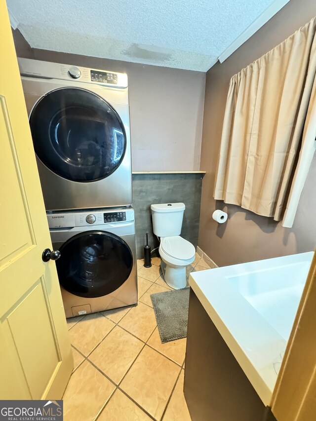 bathroom with stacked washer and dryer, vanity, toilet, tile patterned floors, and a textured ceiling