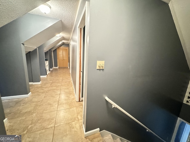 hallway with light tile patterned flooring, lofted ceiling, and a textured ceiling