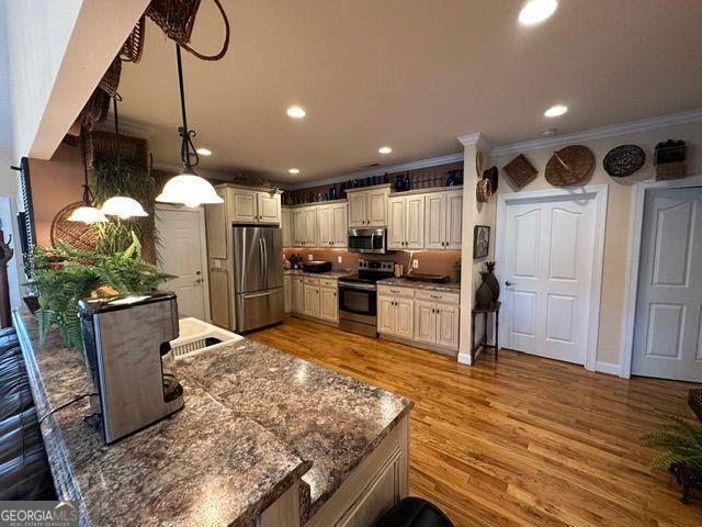 kitchen with crown molding, stainless steel appliances, cream cabinets, decorative light fixtures, and light wood-type flooring