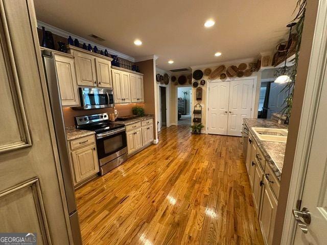 kitchen with ornamental molding, appliances with stainless steel finishes, light stone counters, and light wood-type flooring