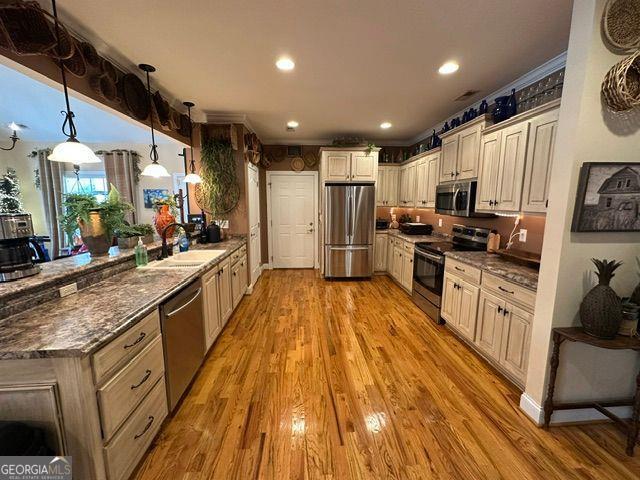 kitchen featuring sink, appliances with stainless steel finishes, dark stone countertops, light hardwood / wood-style floors, and decorative light fixtures