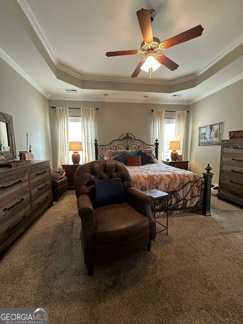 carpeted bedroom with crown molding, a tray ceiling, and ceiling fan