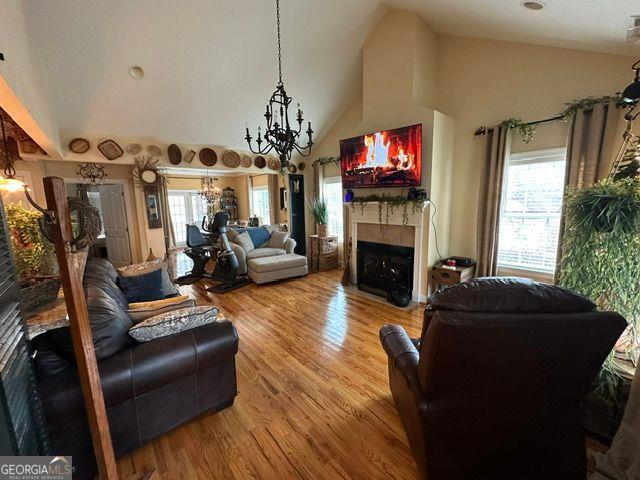 living room with an inviting chandelier, high vaulted ceiling, plenty of natural light, and hardwood / wood-style floors