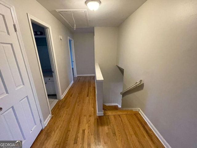 hallway with light wood-type flooring, attic access, baseboards, and an upstairs landing