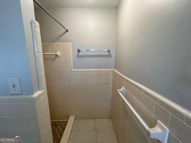 full bath with a wainscoted wall, a stall shower, tile patterned flooring, and tile walls