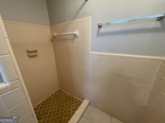 bathroom with tiled shower, wainscoting, tile walls, and tile patterned floors