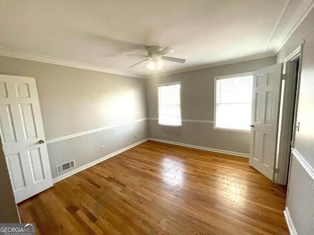 empty room featuring a wainscoted wall, ceiling fan, ornamental molding, and wood finished floors