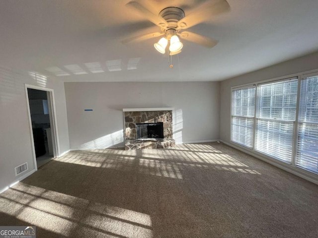 unfurnished living room featuring carpet floors, visible vents, a ceiling fan, a stone fireplace, and baseboards