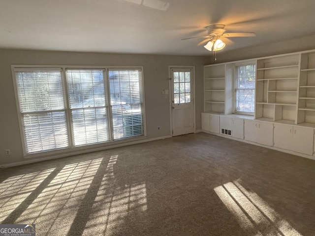 interior space with dark colored carpet, a ceiling fan, visible vents, and baseboards