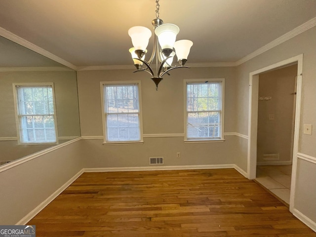 unfurnished dining area with baseboards, visible vents, ornamental molding, wood finished floors, and a chandelier