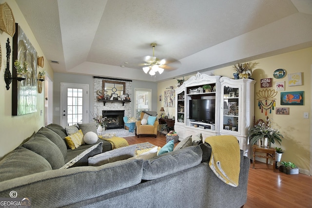 living room with hardwood / wood-style flooring, ceiling fan, a fireplace, a textured ceiling, and a raised ceiling