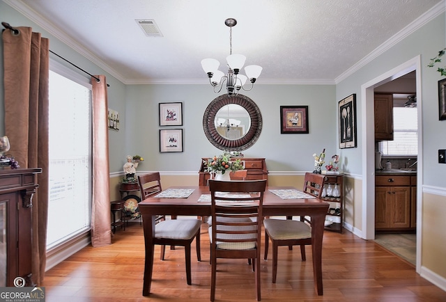 dining space with an inviting chandelier, a wealth of natural light, light hardwood / wood-style flooring, and ornamental molding