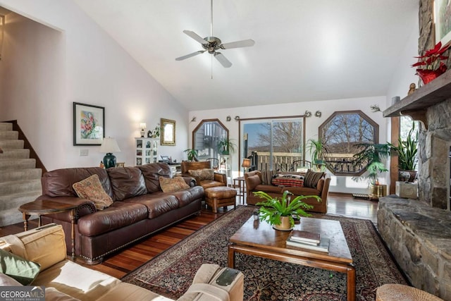 living room featuring hardwood / wood-style flooring, ceiling fan, a stone fireplace, and high vaulted ceiling