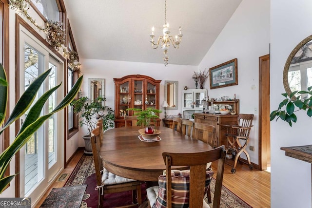 dining area with a notable chandelier, hardwood / wood-style flooring, a wealth of natural light, and high vaulted ceiling