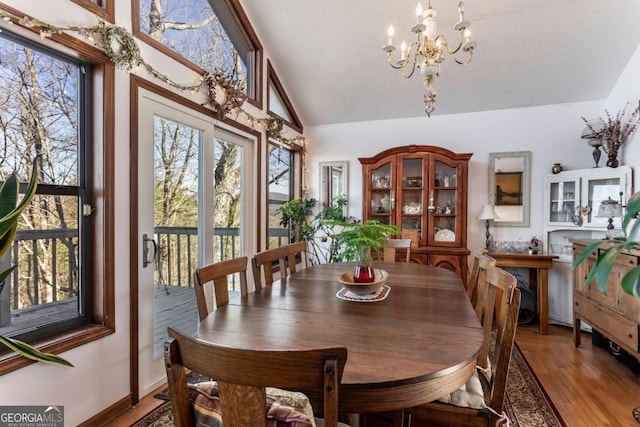 dining room featuring lofted ceiling, hardwood / wood-style floors, a notable chandelier, and a textured ceiling