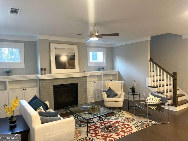 living room featuring ceiling fan, a fireplace, ornamental molding, and dark hardwood / wood-style flooring