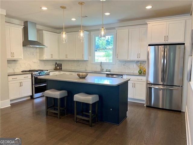 kitchen featuring white cabinets, stainless steel appliances, a kitchen island, and wall chimney range hood