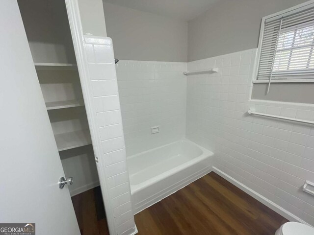 bathroom with tile walls, wood-type flooring, bathtub / shower combination, and toilet