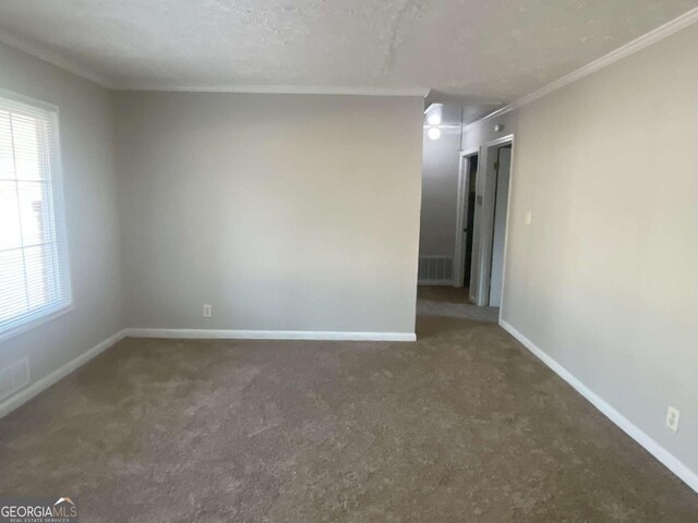 empty room featuring crown molding, a textured ceiling, and dark carpet