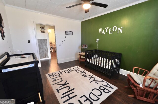 bedroom with a crib, crown molding, and dark hardwood / wood-style flooring