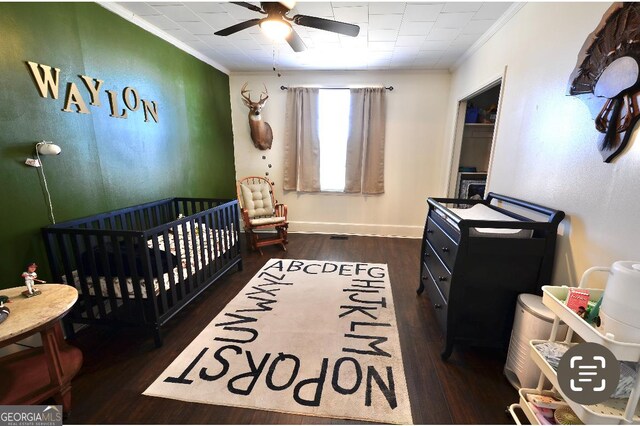 bedroom with ceiling fan, ornamental molding, dark hardwood / wood-style floors, and a nursery area