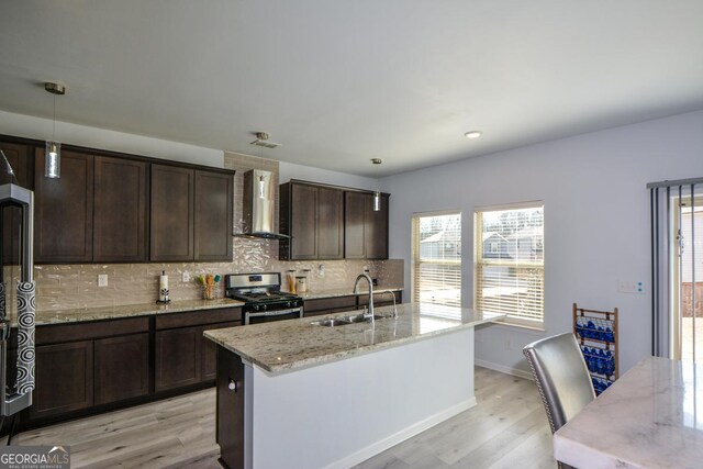 kitchen featuring stainless steel range with gas cooktop, decorative light fixtures, sink, light stone countertops, and wall chimney exhaust hood