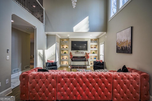 living room with hardwood / wood-style floors, a towering ceiling, ornamental molding, and built in shelves