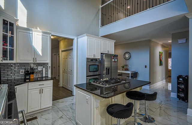 kitchen with a breakfast bar area, white cabinetry, a center island, ornamental molding, and appliances with stainless steel finishes