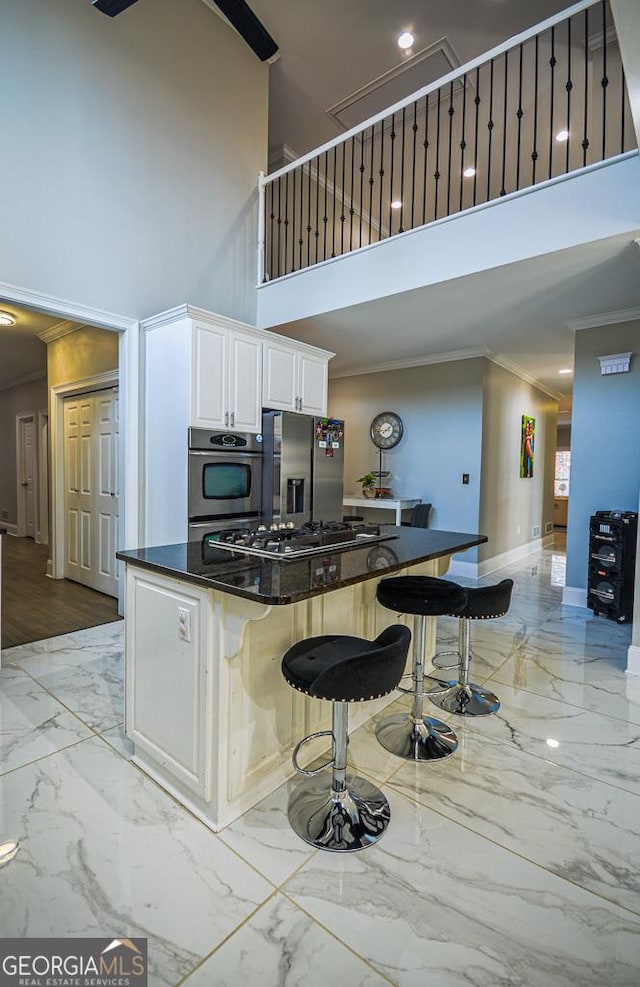 kitchen featuring appliances with stainless steel finishes, a towering ceiling, white cabinets, a kitchen bar, and crown molding