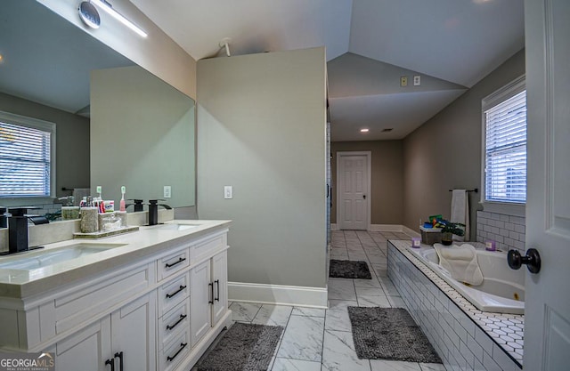 bathroom with vaulted ceiling, plenty of natural light, tiled bath, and vanity