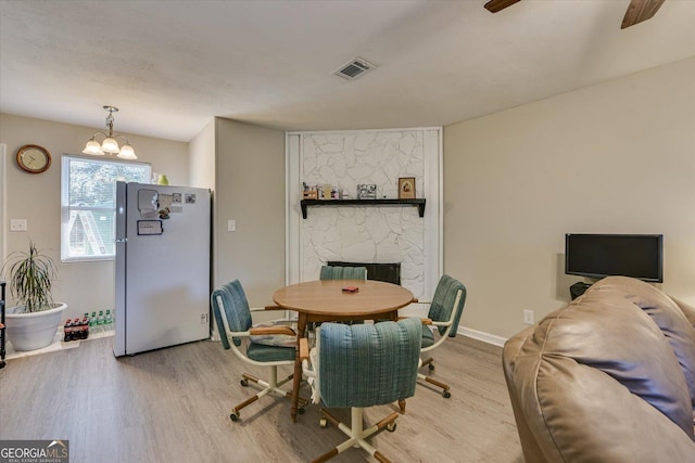 dining area with ceiling fan with notable chandelier, a fireplace, and light hardwood / wood-style flooring