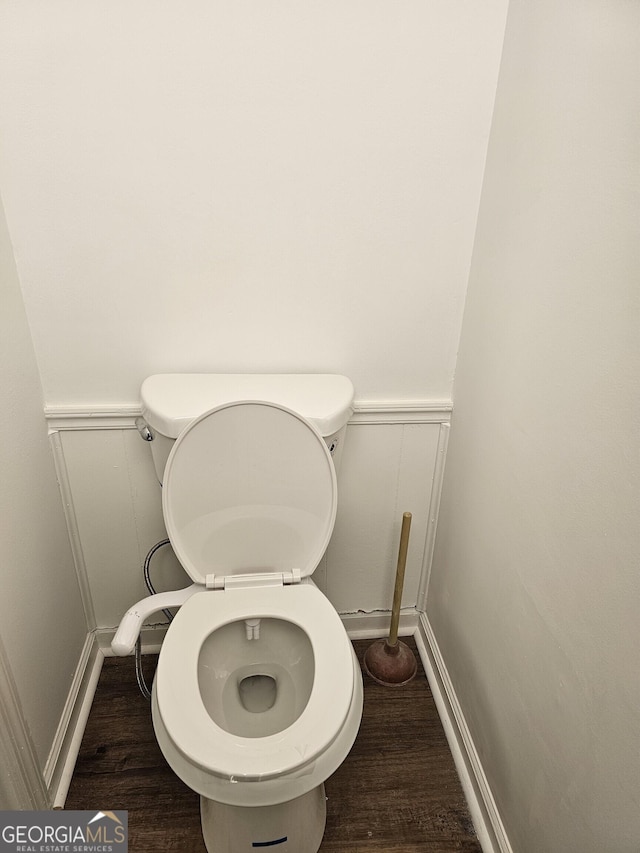 bathroom with a wainscoted wall, toilet, and wood finished floors