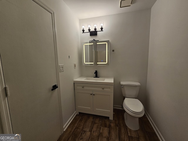 bathroom with baseboards, toilet, wood finished floors, and vanity