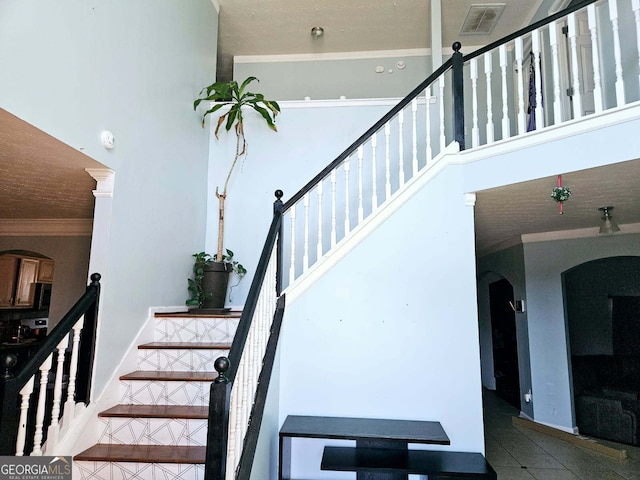 stairway with crown molding, a towering ceiling, and tile patterned flooring