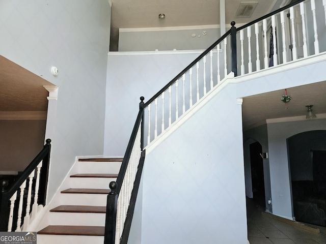 stairway with crown molding, tile patterned flooring, and a high ceiling